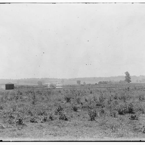 Long-range view of machine on launching track, showing hangar nearby and hummocky ground of former swamp at Huffman Prairie, Dayton, Ohio Long-range view of machine on launching track, showing hangar nearby and hummocky ground of former swamp at Huffman Prairie, summer 1904.